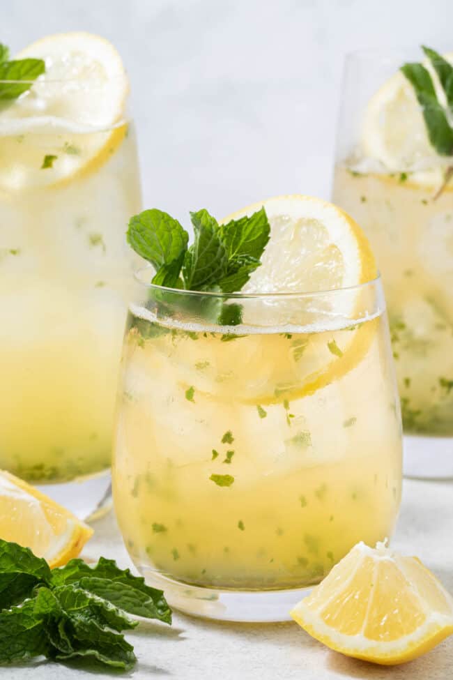 Three clear glasses filled with iced lemon mint green tea. The glasses are garnished with lemon slices and sprigs of fresh mint.