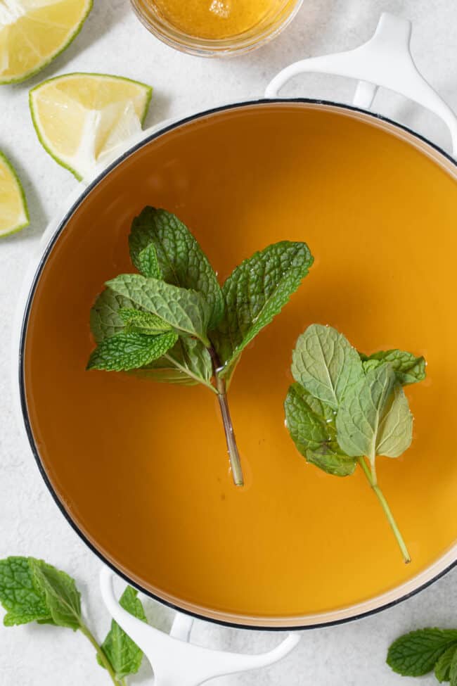 A white pot filled with liquid and sprigs of fresh herbs.