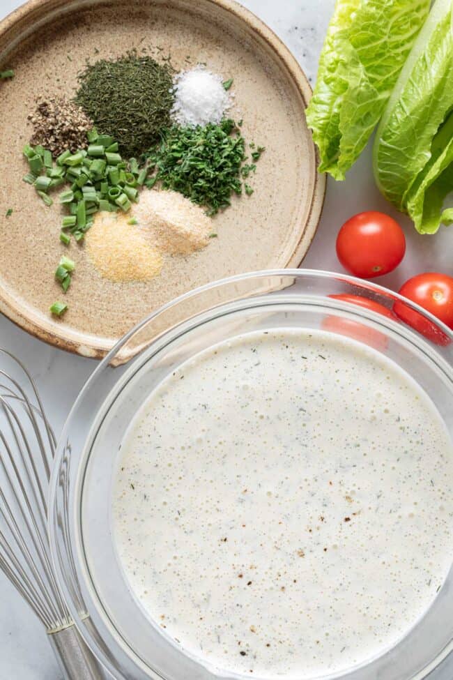 A tan colored plat has small scoops of spices sits next to a mixing bowl filled with while liquid. Radishes and lettuce sit next to the bowl.