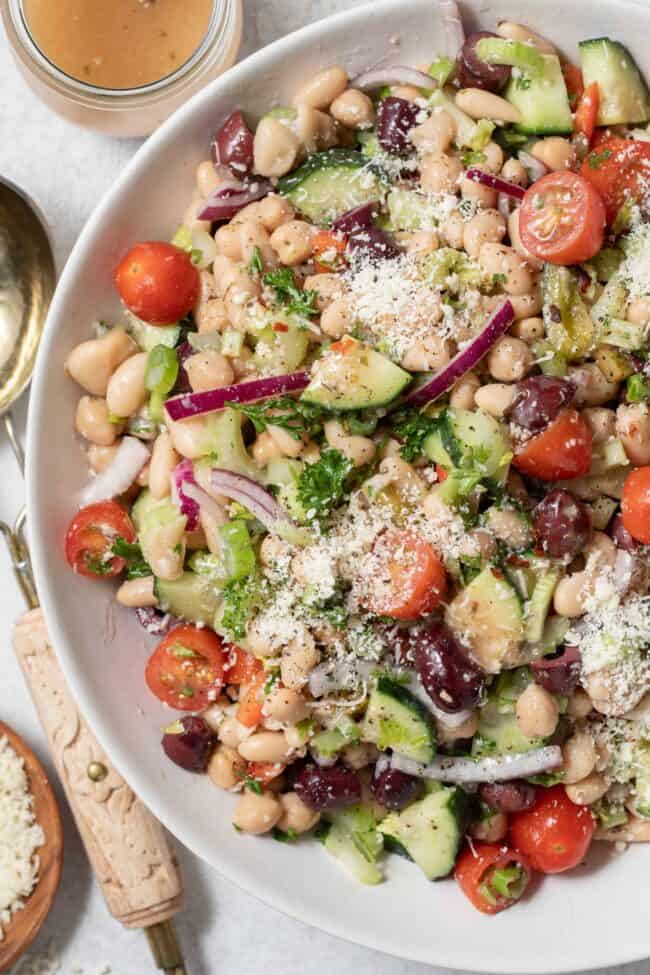 A large white salad bowl filled with legumes and chopped vegetables tossed in a dressing.