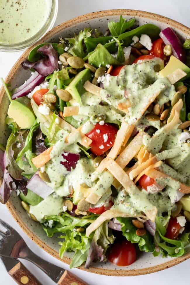 A tan colored bowl filled with salad tossed with green dressing.