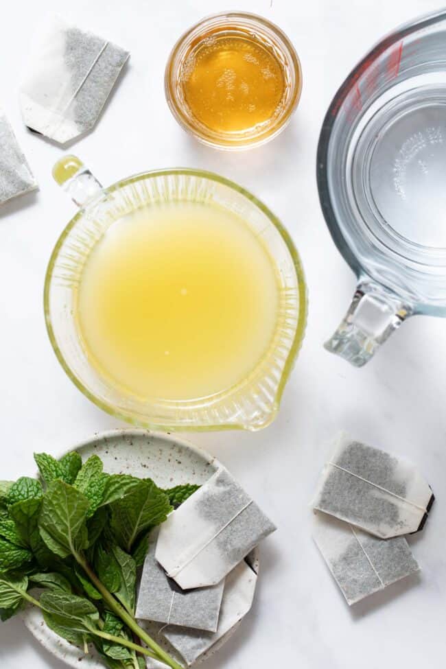 Two clear glass measuring cups - one filled with juice and the other filled with water. Next to these cups sits a small clear glass bowl filled with hoey.