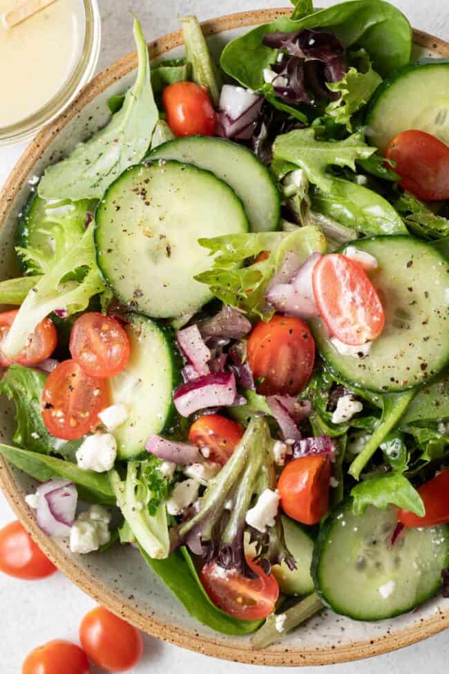 A tan colored bowl filled with salad tossed with vinaigrette.