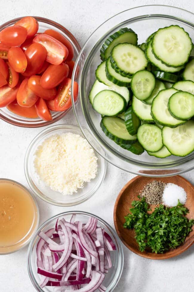 Clear glass mixing bowls filled with vegetables, salad dressing and herbs.