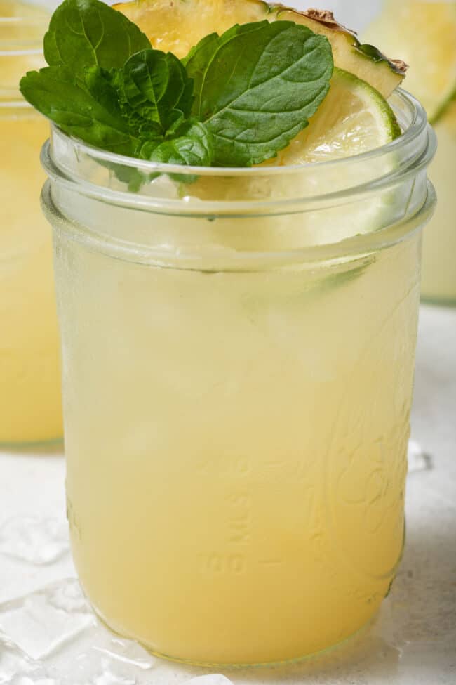 A clear glass mason jar filled with liquid and ice. Lime slices garish the drink.