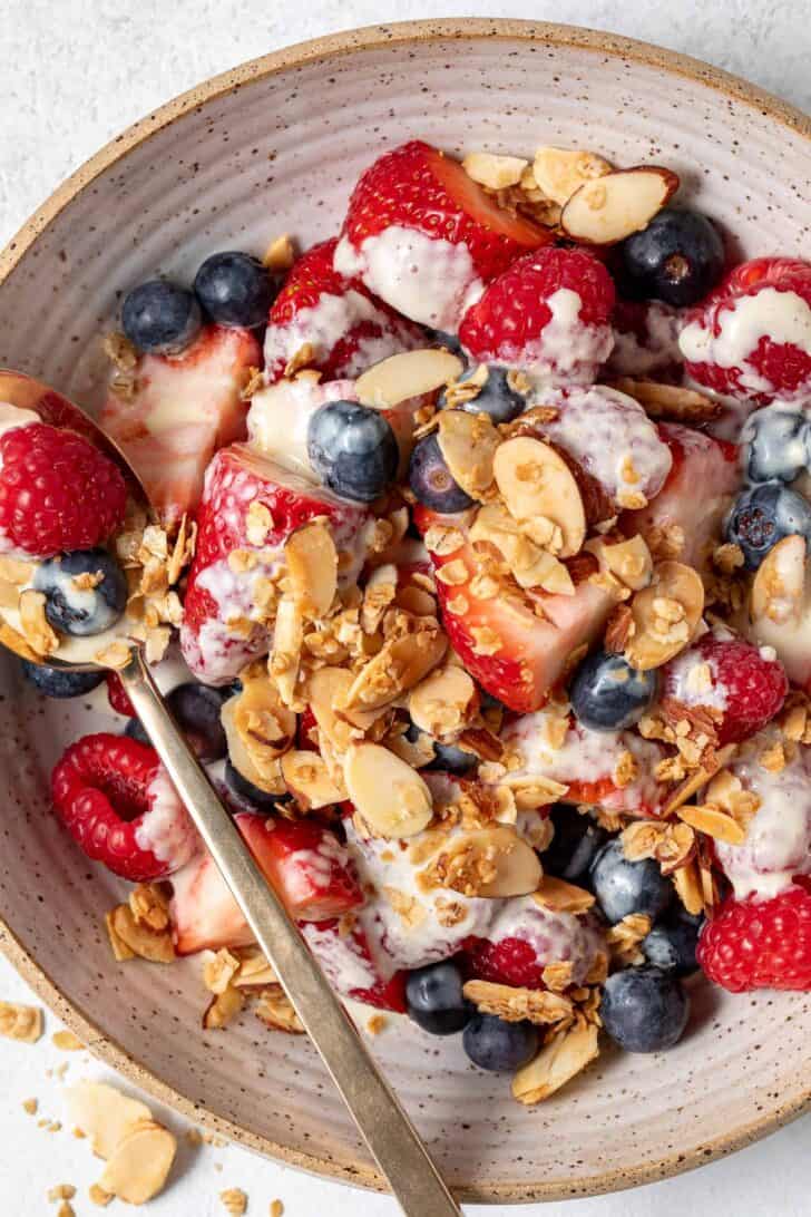 A tan colored bowl filled with mixed berries, toasted nuts and granola.