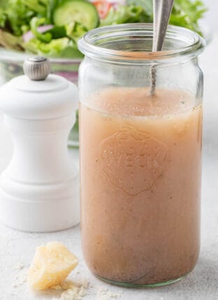 A clear glass mason jar filled with Red Wine Vinaigrette dressing. A salad sits behind the jar.