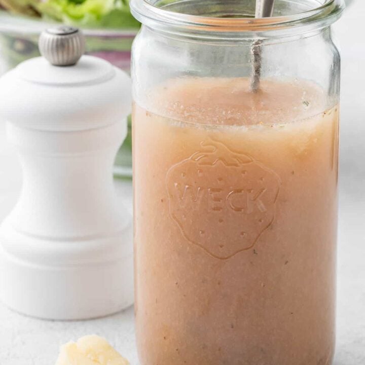 A clear glass mason jar filled with Red Wine Vinaigrette dressing. A salad sits behind the jar.