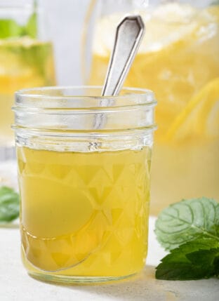 A clear glass mason jar filled with honey mint simple syrup. Fresh mint leaves sit next to the jar.