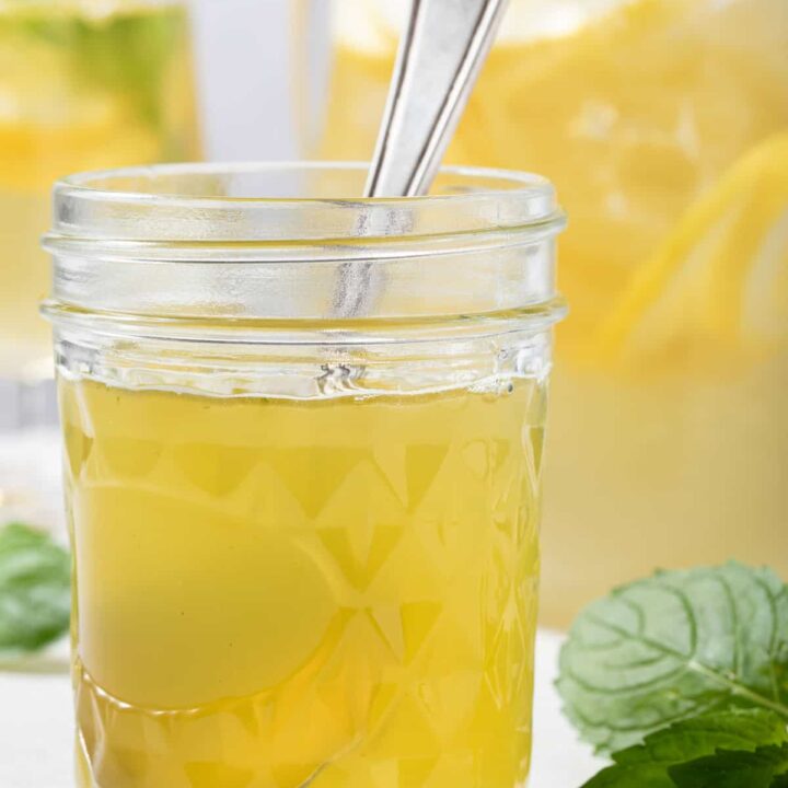 A clear glass mason jar filled with honey mint simple syrup. Fresh mint leaves sit next to the jar.