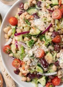 A large white salad bowl filled with legumes and chopped vegetables tossed in a dressing.