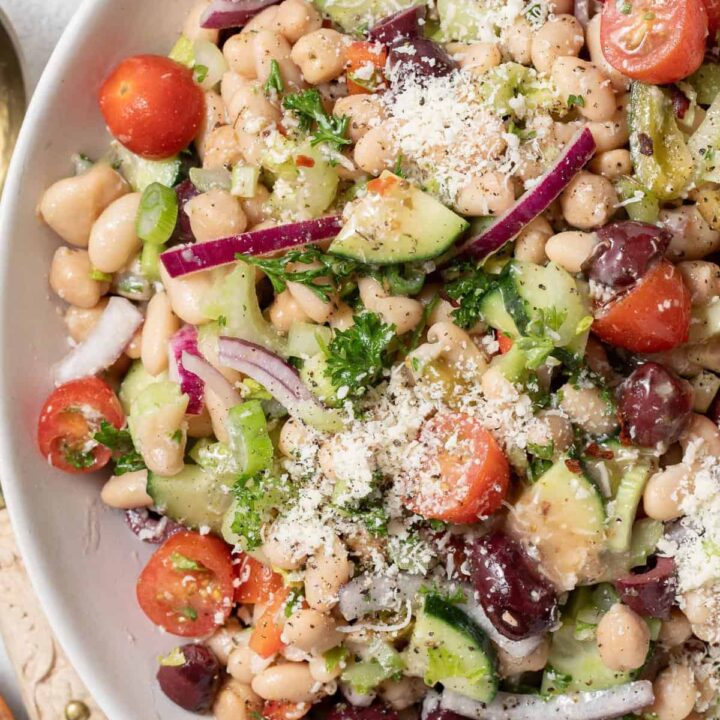 A large white salad bowl filled with legumes and chopped vegetables tossed in a dressing.