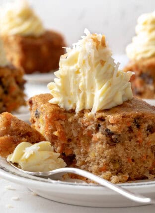 Three white plates with pieces of carrot cake on them. A fork rests on one of the plates.