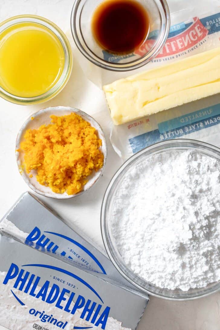 Two sticks of cream cheese next to a stick of butter and a small glass bowl filled with powdered sugar.