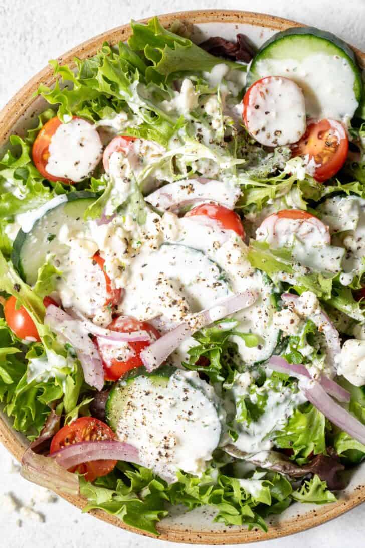 A tan colored bowl filled with mixed greens, cherry tomatoes, sliced onion and cucumber.