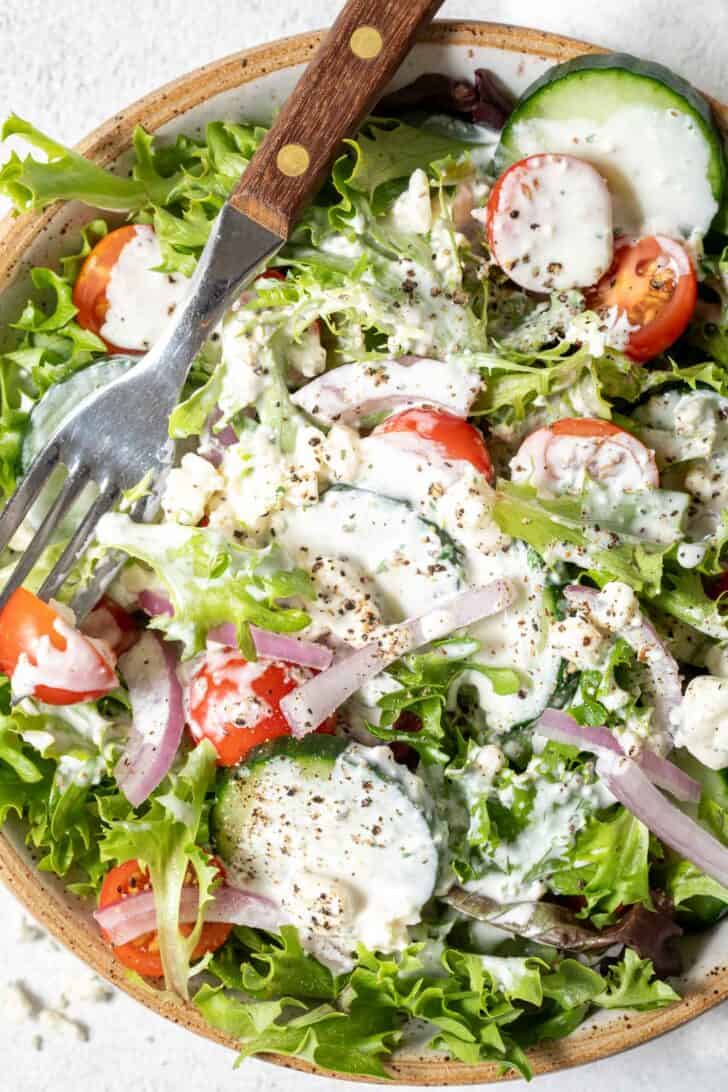A tan colored bowl filled with mixed greens, cherry tomatoes, onion and sliced cucumbers.