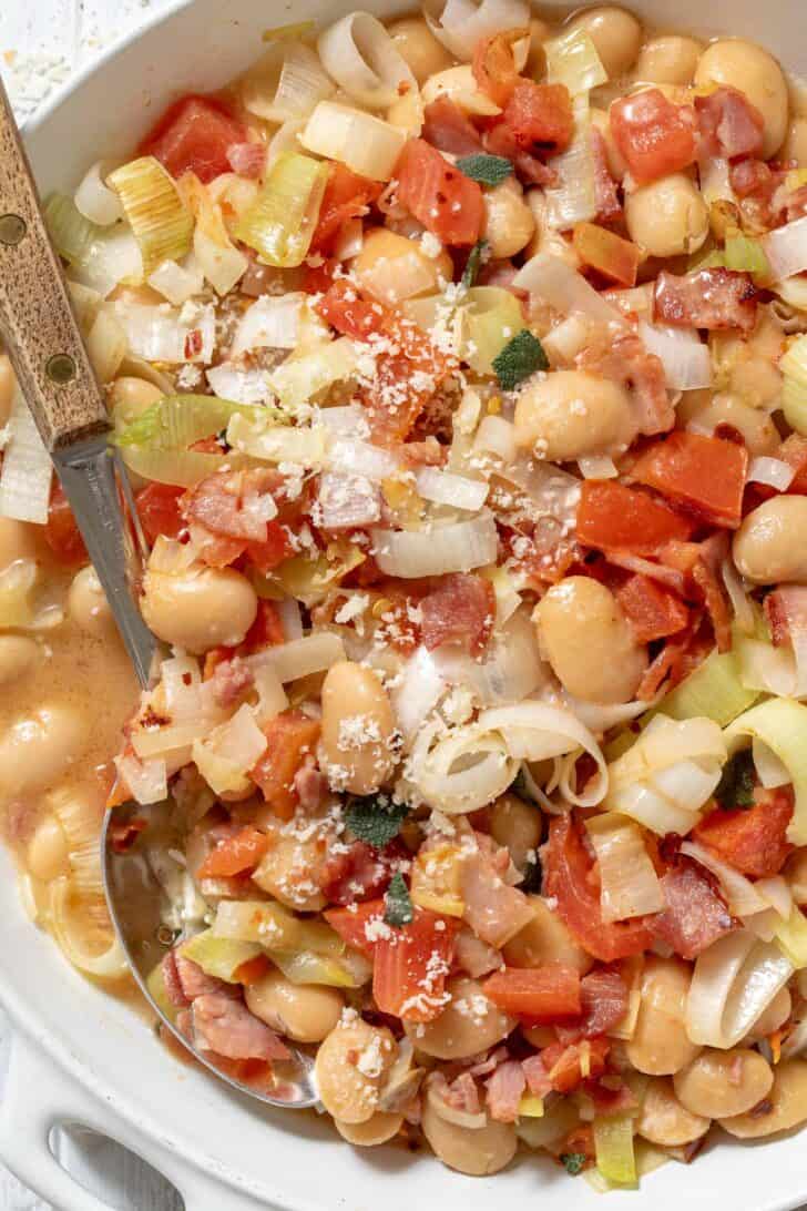 A white skillet filled with Butter Beans. A serving spoon rests in the skillet.