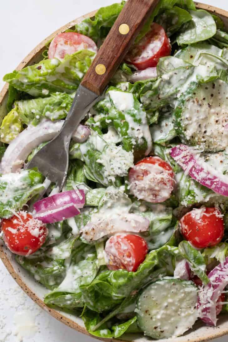 A tan colored bowl filled with mixed greens, cherry tomatoes and red onion.