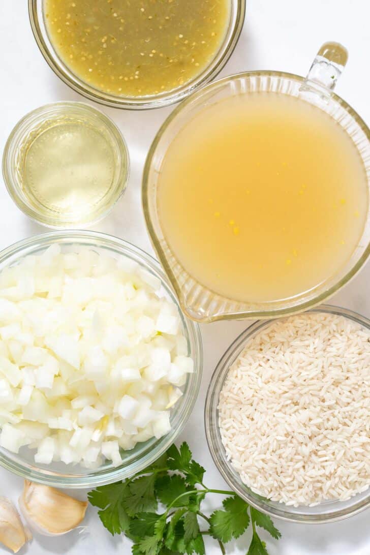 Clear glass measuring cups filled with white rice, chopped onion, salsa verde and chicken broth.