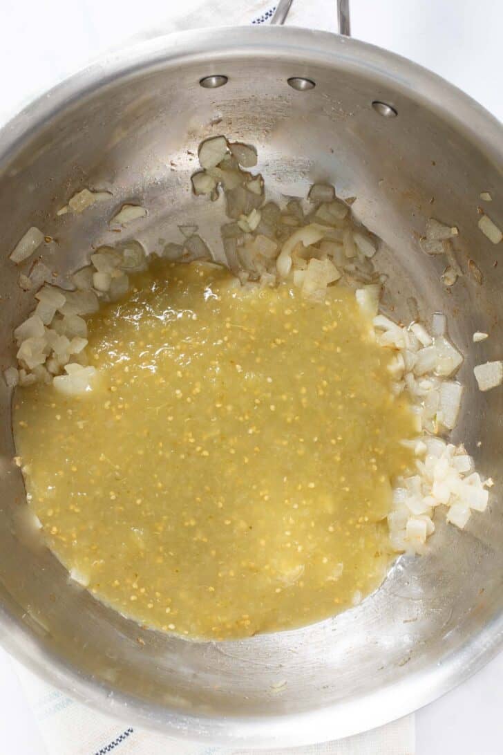 A pot with sauteed onion and salsa verde.