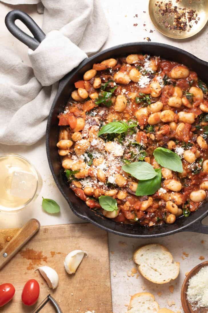 A cast iron skillet filled with Italian Butter Beans (for an Italian butter bean recipe). A cream colored dish towel is wrapped around the handle of the skillet.