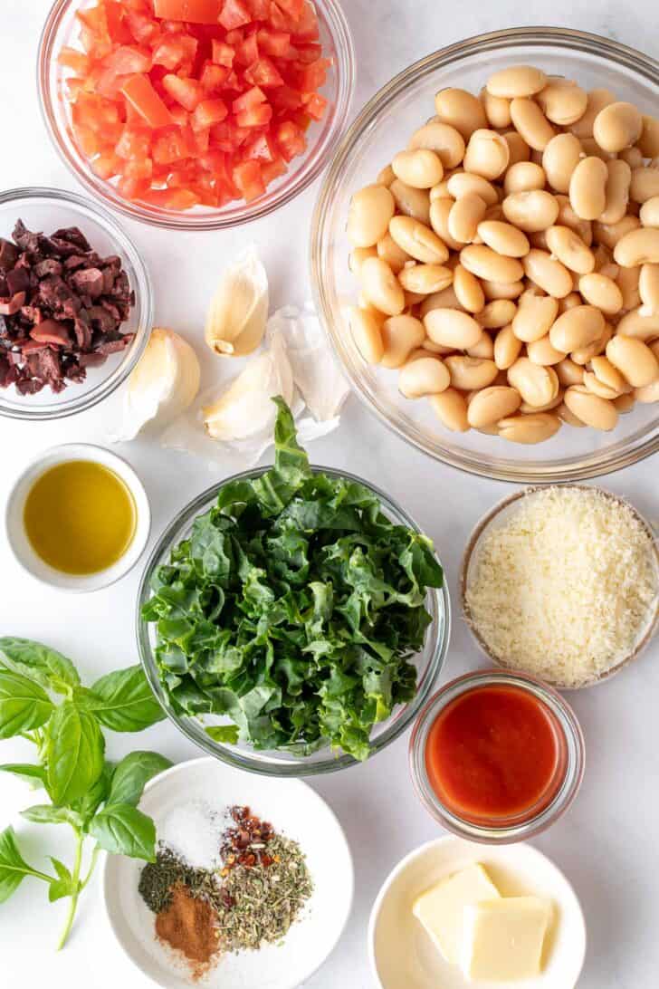 Four small glass bowls filled with legumes, kale, tomatoes and kalamata olives.