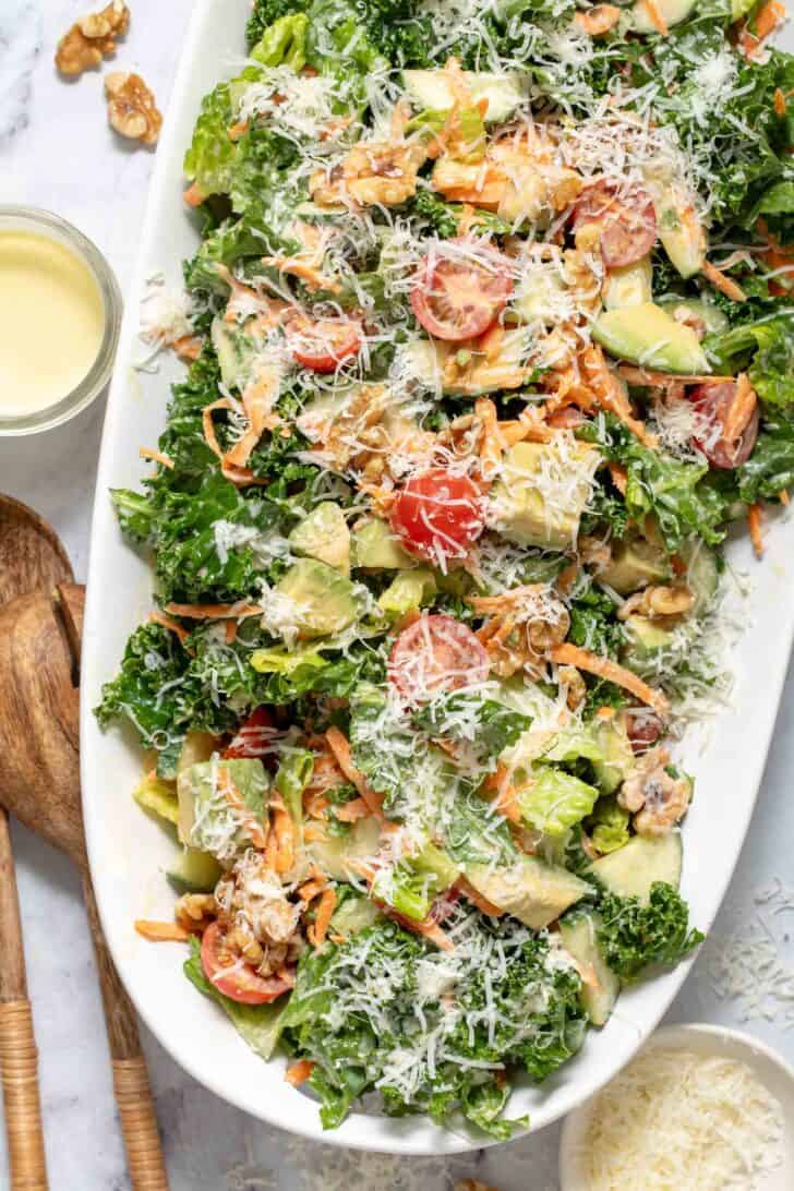 A white platter filled with Lemon Kale Salad. A pair of wooden salad servers sit next to the platter.