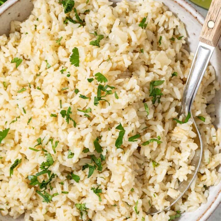 A tan colored bowl filled with Mexican Green Rice. A serving spoon rests in the bowl.