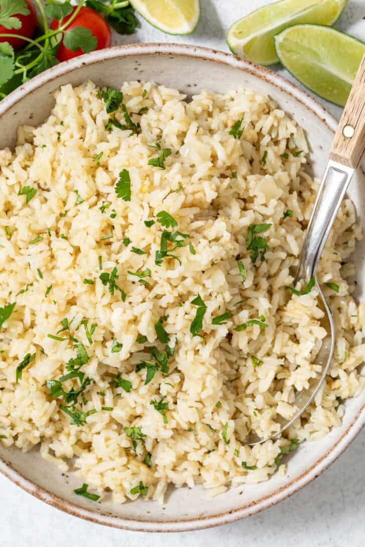 A tan colored bowl filled with Mexican Green Rice. A serving spoon with a wooden handle rests in the bowl.