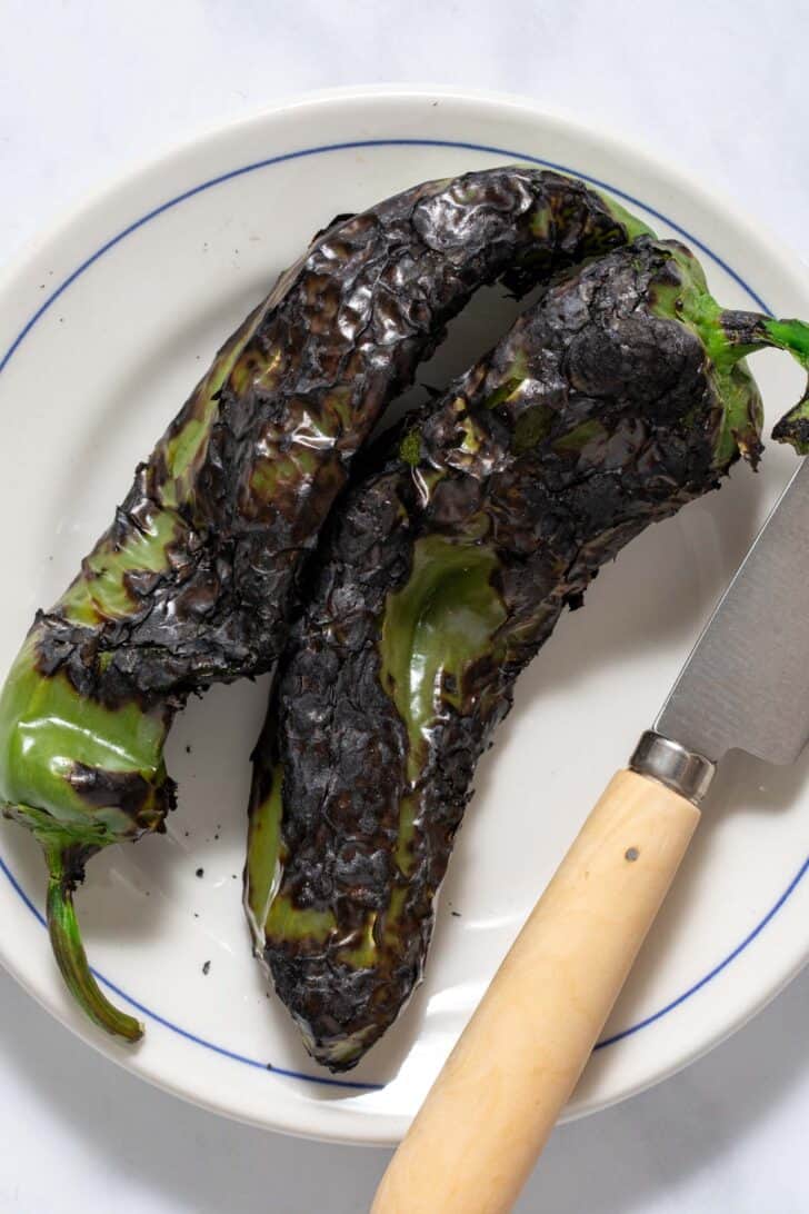 A white plate with two roasted Anaheim peppers on it.