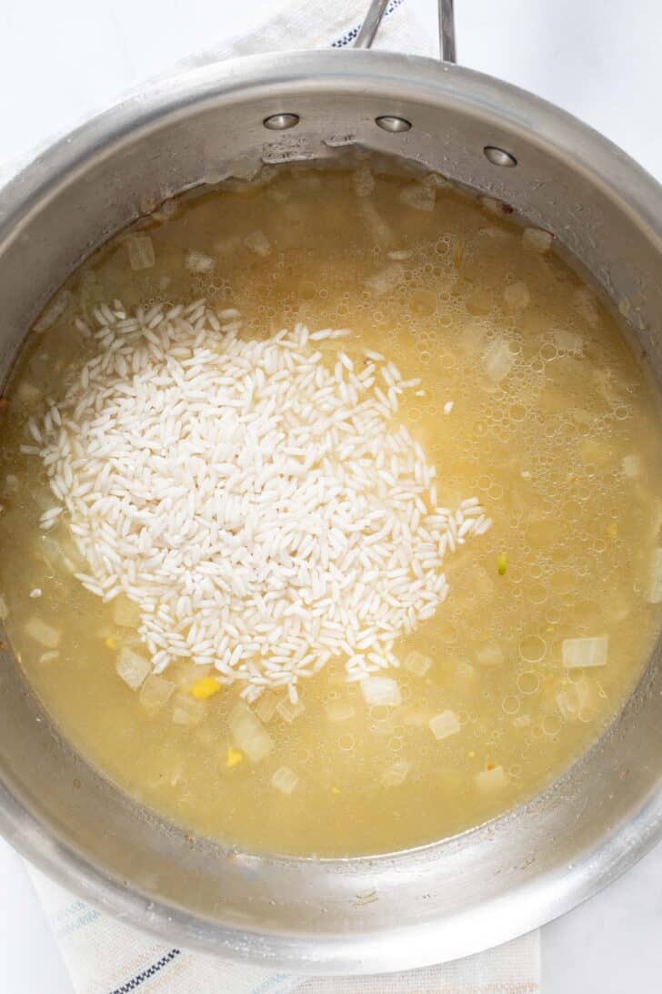 A pot filled with chicken broth, rice, cooked onion and salsa verde.