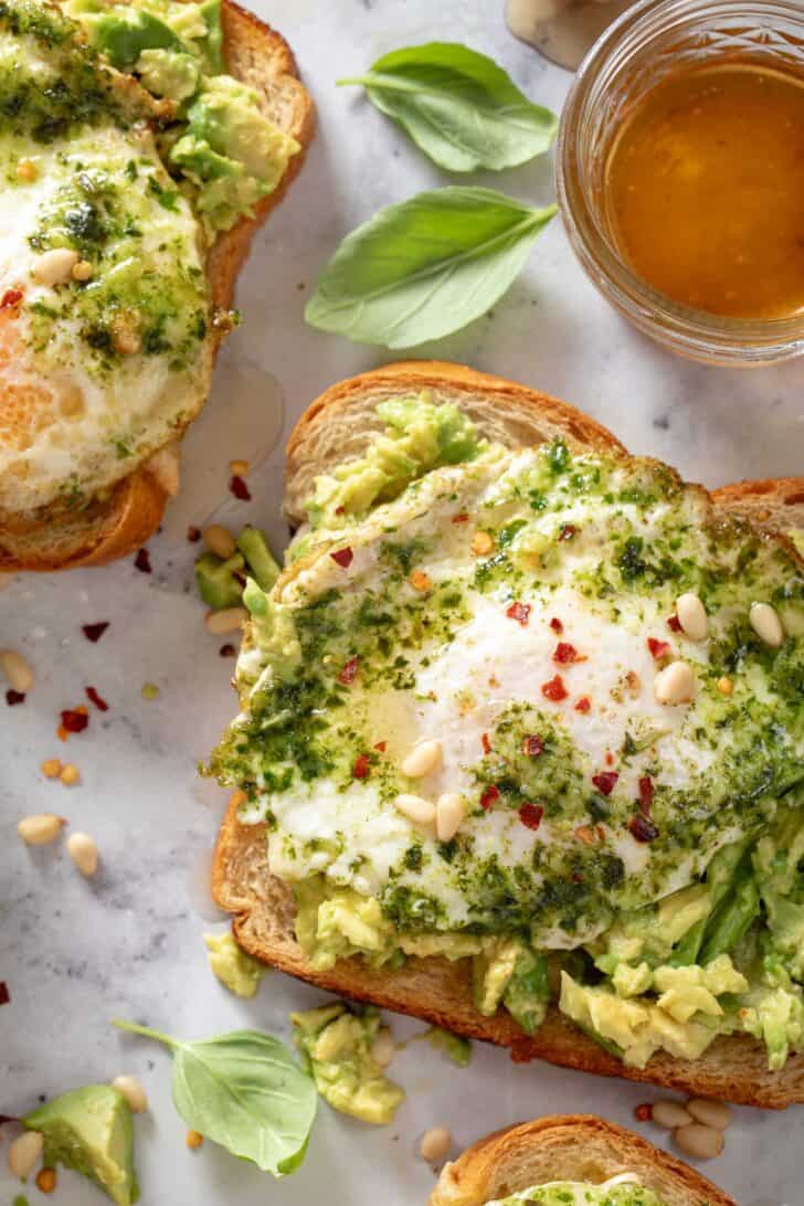 Two pieces of bread with green sauce on top. A jar of honey sits next to the bread.