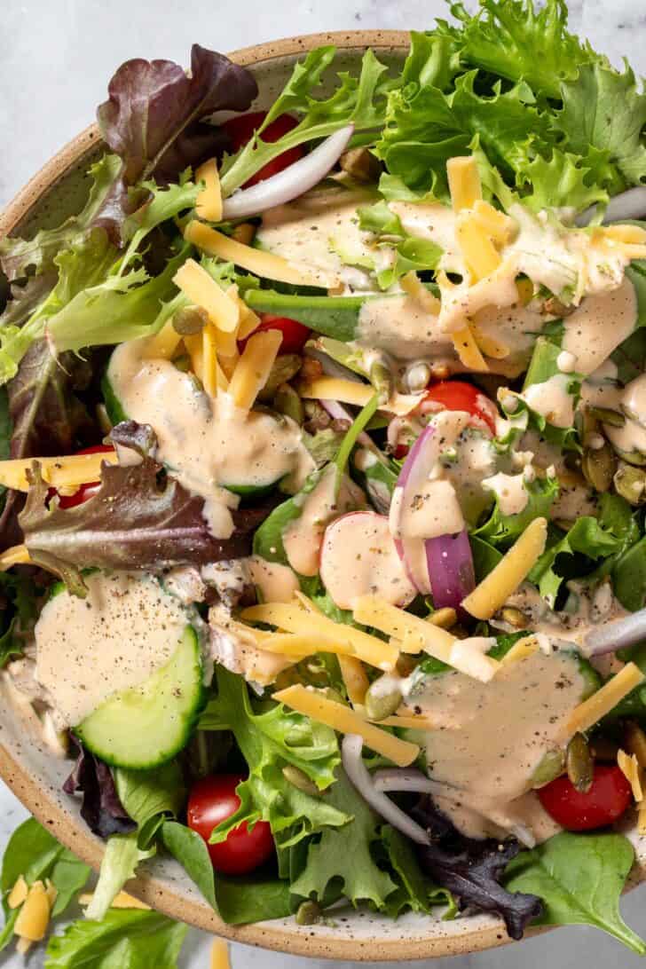 A tan colored bowl filled with mixed greens and cucumber and tomato slices.