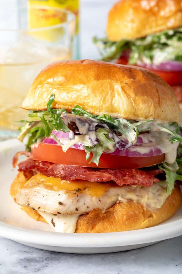 A Grilled Chicken Sandwich sits on a white plate. A second sandwich sits behind it.