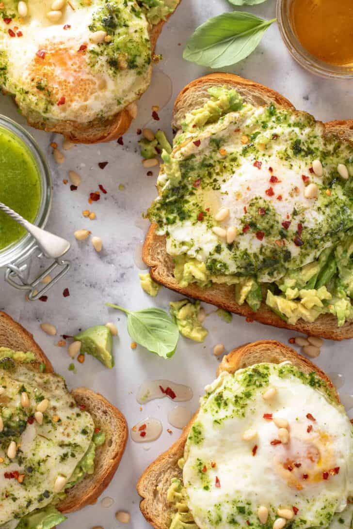 This Pesto Eggs Avocado Toast recipe is made with mashed avocado on your favorite toasted bread, topped with fried pesto eggs drizzled with honey. Avocado toast with egg is great for breakfast, lunch or as a light dinner! 