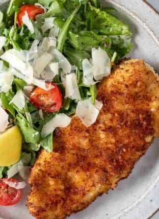 A white plate filled with arugula salad and Easy Parmesan Crusted Chicken cutlets.