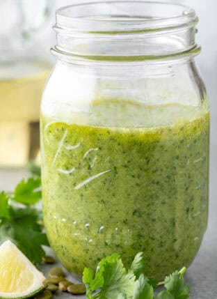 A clear glass mason jar filled with Cilantro Pesto. A spoon rests in the jar.