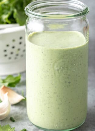 A clear mason jar filled with Homemade Green Goddess Dressing.
