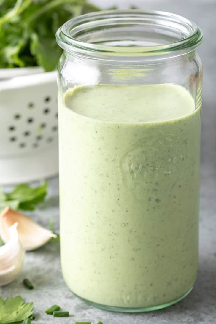 A clear mason jar filled with Homemade Green Goddess Dressing.