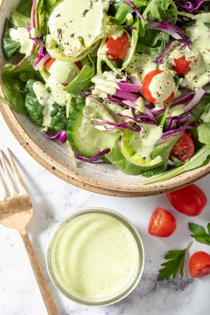 A bowl of salad tossed with Homemade Green Goddess Salad Dressing.