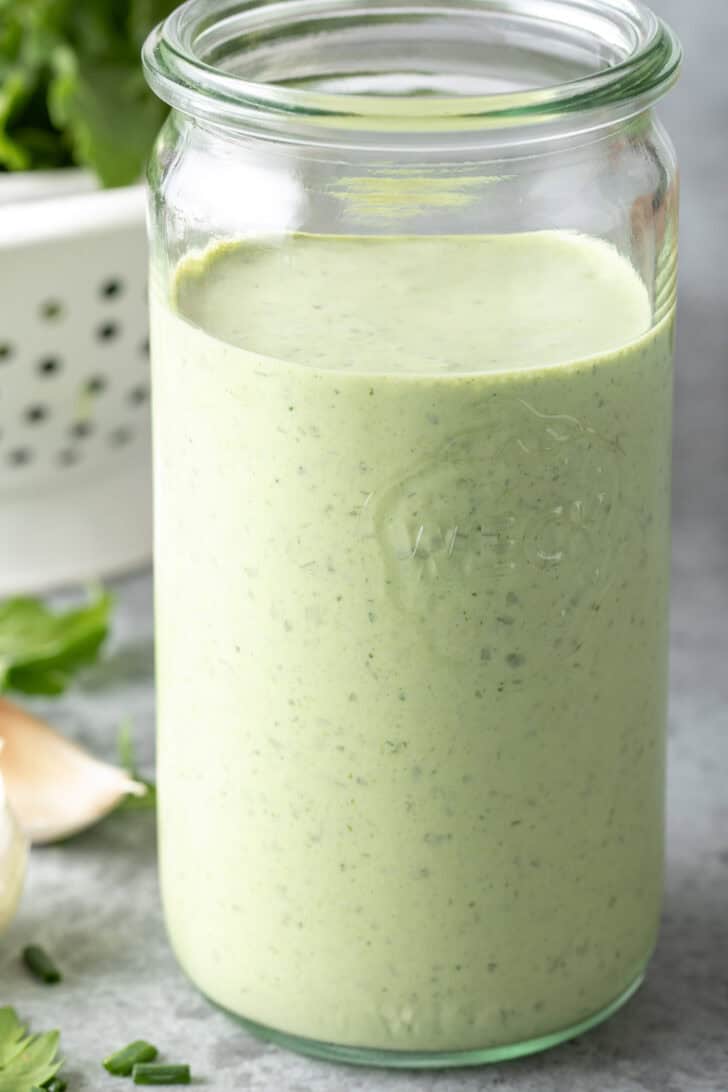 A clear mason jar filled with Green Goddess Dressing.