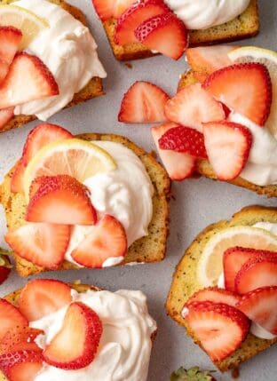 Slices of pound cake topped with Mascarpone Whipped Cream. Slices of strawberries are scattered over the cream.