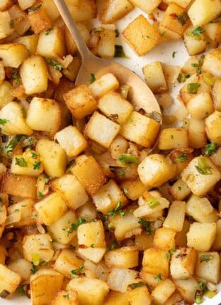 A white skillet filled with crispy breakfast potatoes.