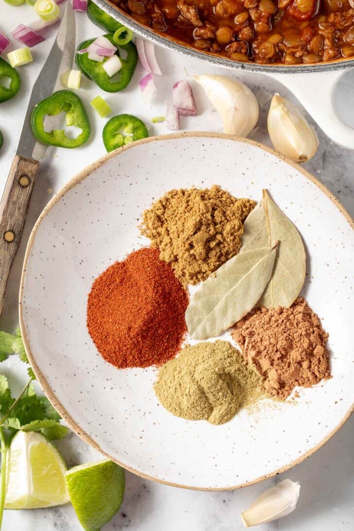 A small dish of the best chili seasoning recipe ingredients sits next to a pot of lentil chili.