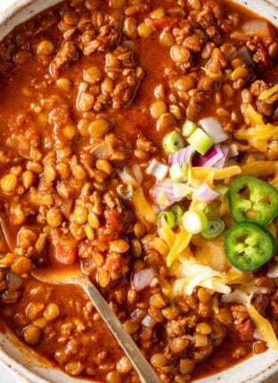 A bowl filled with turkey Lentil chili garnished with cheese and slices of jalapeno.