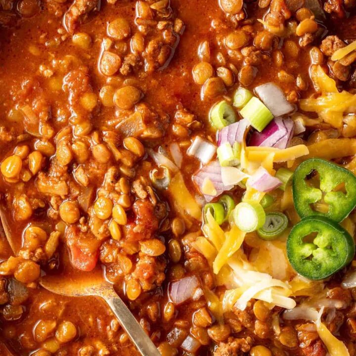 A bowl filled with turkey Lentil chili garnished with cheese and slices of jalapeno.
