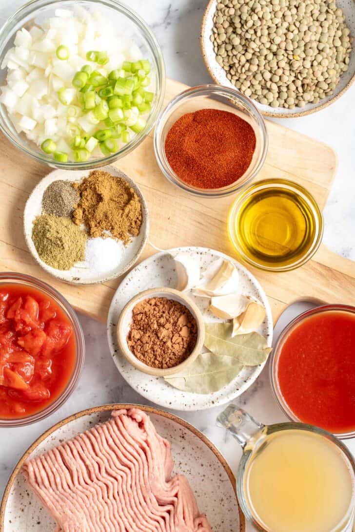 Bowls filled with ground meat, spices, canned tomatoes, olive oil and chopped onion.