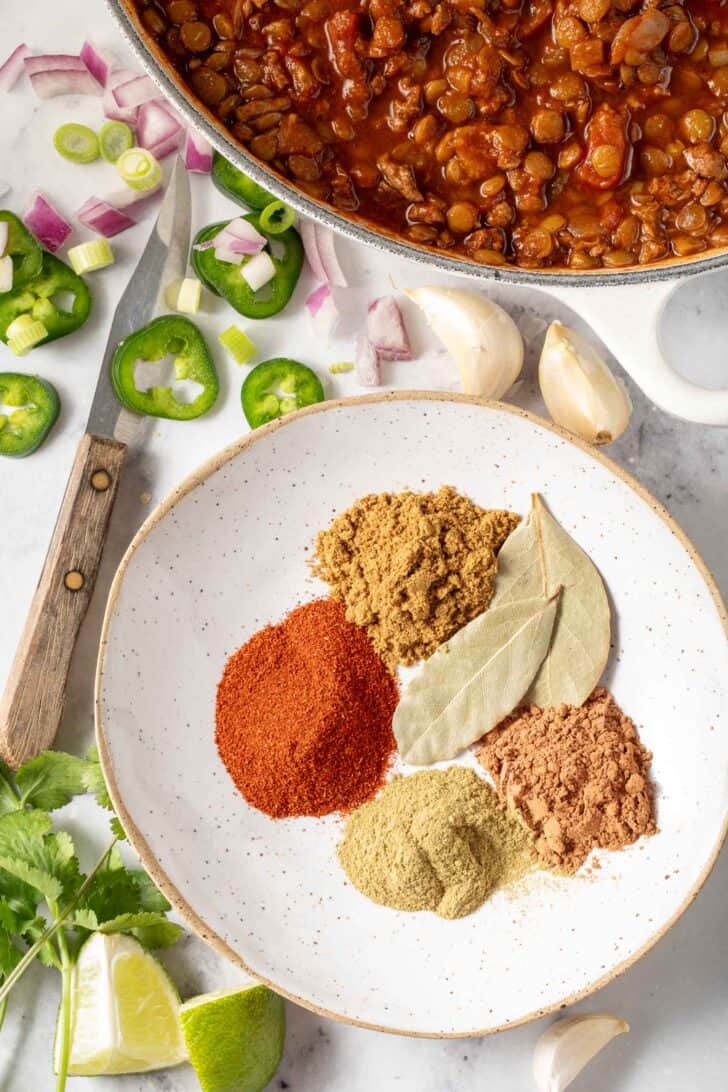 A white dish of spices next to a pot of cooked lentils.