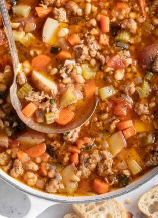 A white Dutch Oven filled with Sausage Kale White Bean Soup.