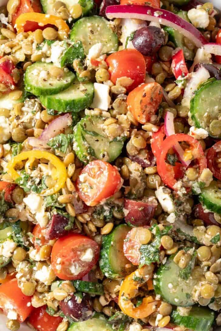 A bowl filled with Greek Lentil Salad made with cooked lentils, sliced cucumbers, tomatoes, red onion, sweet peppers, kalamata olives and Feta cheese.